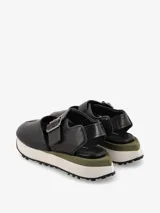 Sandalia de cuero color negro, con tira ancha sobre el empeine con hebilla metálica ajustable, talón cubierto y plataforma con base de goma blanca y suela dentada.