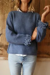 Buzo tejido en punto arroz color azul, con cuello redondo y detalle de flecos en los puños. Presenta un diseño holgado de manga larga y largo hasta la cadera.