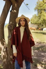 Ruana tejida en lana merino color bordó, con diseño de punto texturizado y terminación de flecos en el ruedo.