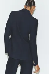 Blazer de cuello solapa y manga larga con cierre frontal de un botón. Presenta bolsillos delanteros con solapa y diseño estructurado.