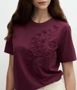 Remera de algodón con cuello redondo y mangas cortas, caracterizada por un bordado floral en relieve aplicado en el frente.