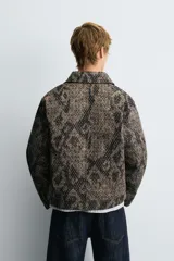Cazadora de corte relajado confeccionada en tejido compacto con textura jacquard. Presenta cuello solapa, cierre frontal con cremallera, manga larga con puños ajustables mediante botones a presión, bolsillo con cierre en el pecho y bolsillos laterales de doble vivo.