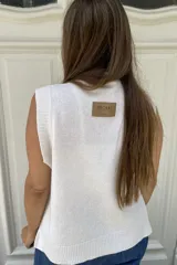 Chaleco de lana color crema con diseño de flor bordada en relieve en el frente, cuello redondo y aberturas laterales en el ruedo.