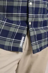 Camisa de manga larga confeccionada en tejido de franela con estampado de cuadros en tonos azul marino y verde. Presenta cuello abotonado, cierre frontal con botones y un bolsillo en el pecho con el logo bordado de la marca.
