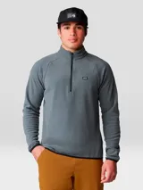 Buzo polar Mountain Hardwear modelo Microchill 1/4 Zip, color gris, con cuello alto, cierre frontal parcial de un cuarto y mangas raglán. Presenta detalles en color negro en los bordes del cuello, puños y ruedo, además de un pequeño logo bordado en el pecho.