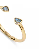 Pulsera rígida dorada de aleación de metales bañada en oro 18k, con dos cristales facetados multicolor en forma triangular en los extremos.