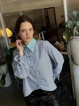 Camisa a rayas verticales azules y blancas, de popelina de algodón, con cuello verde y botones marmolados a tono. Es corta adelante y larga atrás.