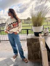 Sweater de punto color crema con diseño geométrico en tonos marrones, naranjas, verdes y grises en el pecho y las mangas. Confeccionado con lana y cuero, con detalles tejidos y bordados a mano.