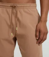 Bermuda deportiva color beige, confeccionada en poliéster, con cintura elástica y cordón de ajuste. Presenta bolsillos laterales y costuras contrastantes.