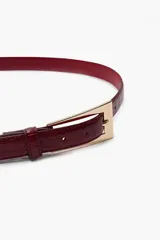 Cinturón de cuero sintético con textura efecto cocodrilo en color bordó, con hebilla metálica rectangular en tono dorado.