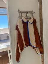 Campera de corderito con diseño de bloques de color, confeccionada en tejido sintético de textura suave. Presenta cierre frontal, cuello alto y ribetes en contraste en los bordes.