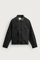 Cazadora relaxed fit de denim de algodón color negro, con cuello de solapa en piel combinada, mangas largas, bolsillos con cremallera en el pecho y cierre frontal con cremallera oculta por solapa con botones.
