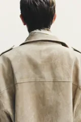 Cazadora de mujer confeccionada en piel de ante color gris oscuro con cuello subido, manga larga con trabillas en los hombros, bolsillos delanteros y con solapa en el pecho. Cierre frontal con cremallera y solapa con botones a presión.