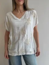 Blusa blanca de corte relajado, con escote en V, mangas cortas amplias y detalles de bordados florales en relieve.
