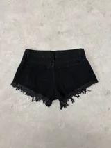 Short de jean negro de tiro bajo con diseño desflecado en los bordes inferiores, bolsillos delanteros y traseros, y cierre frontal con botón y cremallera.