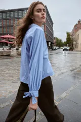 Camisa corta de manga larga, color celeste con finas rayas blancas verticales. Posee cuello solapa y puños anchos ajustados con lazos del mismo tejido.