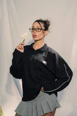 Buzo tipo polo de manga larga, color negro, con cuello y cierre parcial frontal. Presenta un pequeño bordado en el frente y la espalda.