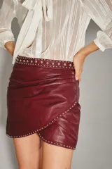 Falda corta cruzada de cuero ovino color bordó, con tachas metálicas plateadas decorando el borde y la cintura.