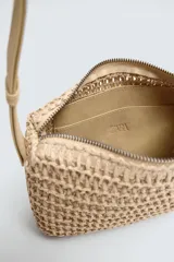Bandolera color beige con acabado trenzado, compartimento principal con cierre de cremallera, bolsillo plano interior y asa de hombro ajustable.