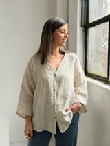 Camisa de lino color beige, de corte holgado, con escote en V y cierre frontal de botones.
