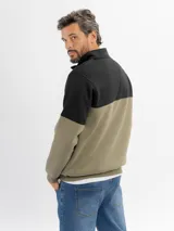 Buzo de felpa con diseño color block, combinando negro en la parte superior y beige en la parte inferior. Presenta cuello alto con cierre frontal parcial y puños elásticos.