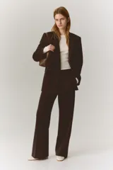 Blazer de color marrón oscuro, de corte ligeramente largo, con solapas de muesca y cierre de doble botonadura con botones oscuros. Presenta hombreras y bolsillos delanteros ribeteados con solapa.