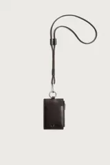 Tarjetero de piel marrón con diseño colgante para el cuello. Cuenta con ranuras para tarjetas, un bolsillo lateral con cierre de cremallera, anilla metálica y cordón largo ajustable.