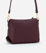 Bolso bandolera pequeño color borgoña, confeccionado en poliuretano con detalle texturizado tejido en la parte inferior. Cuenta con correa transversal ajustable, cierre de cremallera y bolsillo frontal con botón.