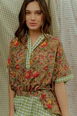 Blusa de algodón con estampado floral multicolor, con detalles en tela a cuadros verde y blanca en el cuello en V, la pechera y los bordes de las mangas cortas.