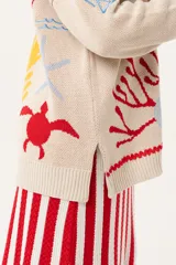 Saco oversize tejido con ilustraciones inspiradas en corales, peces, estrellas de mar y tortugas. Presenta galón picot en rojo en cartera y puños, y botones a tono.