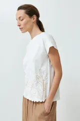 Remera color crudo con bordado de flores en el ruedo y mangas cortas.
