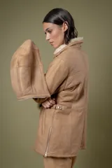 Campera de babylamb color beige con interior de piel sintética al tono. Presenta cierre frontal, capucha desmontable, bolsillos laterales, presillas ajustables en la cintura y cierres en los laterales del ruedo.
