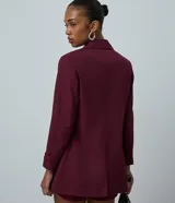 Blazer de sastrería color bordó, de corte oversized y largo, confeccionado en crepé. Presenta solapas clásicas, bolsillos frontales y detalle de pliegues en los puños.