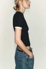 Camiseta blanca de manga corta y cuello redondo, con ribete negro decorado con perlas blancas en el cuello y los puños.