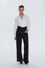 Pantalón de tiro alto, corte recto y pierna amplia, completamente cubierto de lentejuelas negras brillantes.