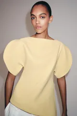 Top amarillo de manga corta abullonada, con cuello barco y bajo asimétrico. Cierre trasero con cremallera oculta.