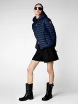 Campera puffer beige con capucha, cierre frontal con cremallera naranja, bolsillos laterales ocultos y logo de goma en la manga. Confeccionada en nylon liviano y con puños y dobladillo elásticos de Lycra.