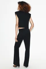 Chaleco corto de Zara con cuello solapa, diseño sin mangas con hombreras y forro interior. Presenta un corte estructurado con cierre frontal mediante botón oculto.