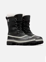 Bota de nieve Sorel modelo Caribou, con diseño impermeable de caña media. Presenta una parte superior de nubuck negro con costuras selladas, cordones frontales y una base de goma vulcanizada resistente. Incluye un forro interior de fieltro y detalle de pelo sintético en el borde superior.