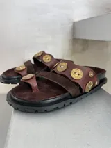 Sandalias marrones de cuero y gamuza, con apliques de monedas doradas.
