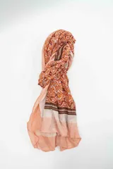Pañuelo rectangular de tejido fino con estampado geométrico y tribal en tonos naranja, terracota y rosa pálido, con bordes en rayas verticales.