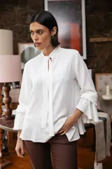 Blusa blanca de textura arrugada, con cuello alto, abertura frontal tipo gota y mangas largas acampanadas con detalle de frunces.