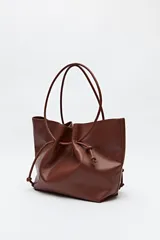 Bolso tipo tote bag negro de cuero sintético, con frunce superior ajustable con cordones y doble asa de hombro.