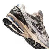 Championes urbanos New Balance modelo 1906, con diseño técnico de estilo retro. Presentan una combinación de malla transpirable y paneles sintéticos en tonos gris, blanco y detalles en azul. Incorporan entresuela con tecnología de amortiguación y suela de goma resistente.