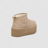 Botas de caña baja tipo botineta con plataforma elevada, confeccionadas en gamuza color marrón. Presentan costuras con detalle de puntada overlock, lengüeta trasera y forro interior de lana suave.