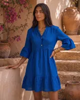 Vestido corto verde militar de lino, con cuello mao, escote en V con botones, mangas tres cuartos acampanadas con volados y falda con volado en el ruedo.