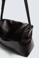 Bolso bandolera de piel color marrón oscuro, con solapa y cierre de imán y cremallera. Incluye un bolsillo interior con cremallera y un bolsillo plano. Tiene asa de hombro ajustable.