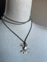 Gargantilla con cordón de gamuza gris y dije de sol dorado con centro de nácar.