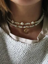 Collar doble de cuentas blancas con detalles dorados, dijes de perlas y dijes de estrellas. El collar inferior tiene un dije de luna dorada.