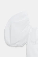 Top blanco de escote cuadrado con fruncidos en el pecho y mangas cortas abullonadas tipo globo. Cuerpo de tejido acanalado ajustado.